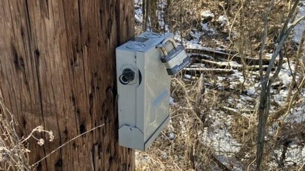 TRAFx infrared trail counter installed on a wooden post in a winter trail environment with padlock security